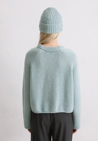 Maglione a maglia blu chiaro con polsini e scollatura a coste, abbinato a un berretto a coste coordinato. Texture morbida e design dal fitting rilassato.