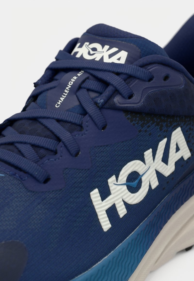 HOKA Challenger sneaker in navy blue with textured upper, contrasting white logo, rounded toe, and a cushioned, textured outsole.