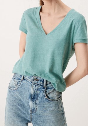 Türkises V-Ausschnitt-T-Shirt aus weichem Material, mit kurzen Ärmeln und lässiger Passform; kombiniert mit hochgeschnittenen, verwaschenen blauen Jeans.