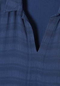 Tissu bleu marine avec des rayures texturées subtiles et un col en V ouvert.