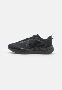 Zapatillas Nike de malla negra y material sintético. Diseño de perfil bajo con una superficie texturizada, cierre con cordones y pestaña trasera para facilitar su puesta.