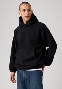 Sort fleece hoodie med en kengurulomme, justerbar snørehætte, ribbede manchetter og en diskret logo-detalje på brystet.