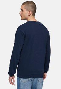 Felpa collo tondo blu navy realizzata in tessuto morbido, caratterizzata da polsini e bordo in costina, con una linea dritta e un logo minimale all'orlo.