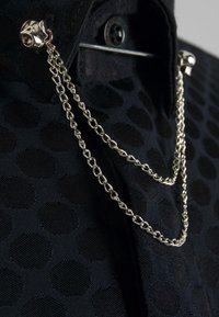 Zwarte gemarmerde stof met cirkelpatronen, voorzien van zilveren kettingen die aan de kraag zijn bevestigd met decoratieve hardwareaccenten.