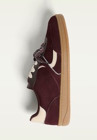 Bordeauxrode sneaker met een gestructureerd suède bovenwerk, crèmekleurige accenten en een rubberen gumzool; voorzien van een afgeronde neus en patroonveters.