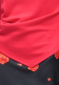 Κόκκινο, απαλό ύφασμα τοπ με άνετη εφαρμογή, συνδυασμένο με μαύρη φούστα που έχει κόκκινα σχέδια με τριαντάφυλλα κατά μήκος του τελειώματος. Ορατές ραφές.