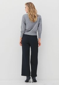 Pilkas megztinis su laisvu kirpimu, apvaliu apačiu ir trijų ketvirčių rankovėmis, derinamas su tamsiomis plačiomis kelnių kelnėmis ir juodais aukštakulniais.