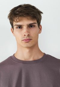 Kurzärmliges T-Shirt mit Rundhalsausschnitt aus sanftem Mauve-Stoff. Glatte Textur mit sichtbaren Nähdetails rund um den Halsausschnitt und die Schultern.