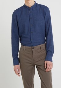 Koszula z długim rękawem w kolorze ciemnoniebieskim, o fakturowanej tkaninie, z przodem zapinanym na guziki i dopasowanymi rękawami, zestawiona z brązowymi spodniami.