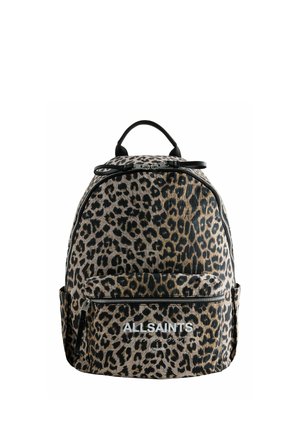 Junge Person trägt einen großen AllSaints-Rucksack mit Leopardenmuster und sichtbarer Front-Reißverschlusstasche vor schlichtem Hintergrund.