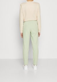 Sudadera beige clara de mangas largas, combinada con pantalones de chándal verde claro con cinturilla elástica y puños acanalados, usados con zapatillas blancas.