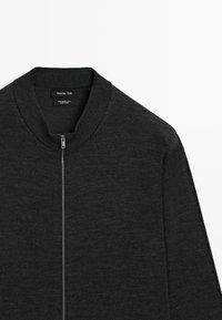 Pull en laine gris foncé, doté d'un col rond et d'une fermeture éclair à l'avant. Texture lisse avec un minimum de détails de couture.