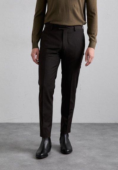 Pantaloni negri, croiți pe corp, asortați cu un top verde cu mânecă lungă și cizme negre până la glezna pe un fundal gri.