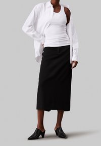Chemise blanche à manches longues sur un débardeur blanc ajusté, associée à une jupe midi noire et des mules en cuir noir. Textures lisses, design minimaliste.