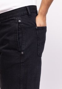 Fekete farmernadrág, slim fit szabással, oldalsó zsebbel, fém részletekkel és sima textúrával. A derékpánt a kényelem érdekében lett tervezve.