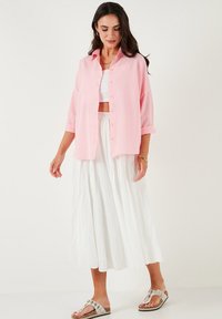 Light pink button-up shirt with rolled sleeves, paired with a white textured maxi skirt and embellished sandals. Minimalist accessories.