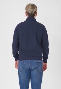 Marineblå, letvægtsjakke med høj krave og lange ærmer, parret med blå denimjeans. Glat overflade uden synlige mønstre.