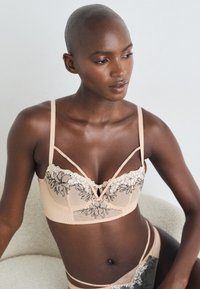 Lett nude bH med blonder, blomsterbroderi, justerbare stropper og krokfeste, dekorert med et teksturert stoff.