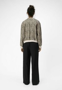 Blouson aviateur à imprimé léopard avec une taille et des poignets côtelés, associé à un pantalon noir à jambes larges. Texture de tissu lisse, coupe décontractée.