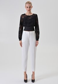 Zwarte doorzichtige top met lange mouwen en bloemenborduursel, gecombineerd met witte op maat gemaakte broek en zwarte hakken. Minimalistisch ontwerp, soepele texturen.