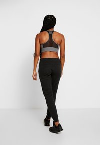 Grauer Sport-BH mit Mesh-Einsatz, kombiniert mit dunkelgrauen Jogginghosen. Das Outfit umfasst schwarze Sportschuhe und zeichnet sich durch eine lockere Passform aus.