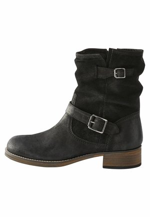 Bottines noires en daim avec un design lâche, boucles en argent, bout rond et un talon en bois empilé. Coutures contrastées le long de la semelle.