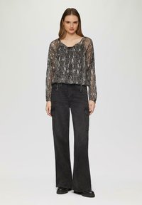 Haut transparent en imprimé serpent noir à manches longues, associé à un pantalon cargo noir taille haute avec poches latérales et une coupe décontractée.