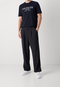 Navy T-shirt with white "HILFIGER NEW YORK EST. 1985" logo, paired with black and white striped, pleated trousers and white sneakers.