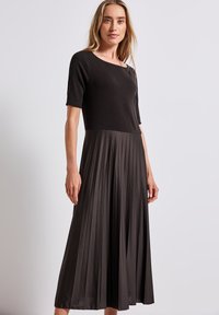 Svart plisserad midi-klänning med korta ärmar, slank bodice och flödande kjol. Tillverkad av mjukt tyg med en jämn textur och minimalistisk design.