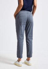 Ljusgrå, avslappnade byxor med elastisk midja, dragsko, muddar vid anklarna och två bakfickor. Tillverkade av mjukt tyg.