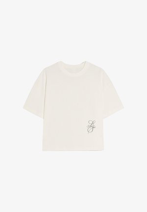 Fehér, rövid ujjú póló kerek nyakkivágással és kis, dőlt betűs "LS" kezdőbetűkkel, a jobb alsó szegély közelében nyomtatva.