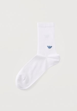 Une chaussette blanche côtelée avec un petit logo d’aigle bleu, sur un fond clair.