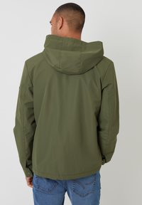 Olivegrüne Kapuzenjacke aus leichtem Material, mit einem lockeren Schnitt, Reißverschlusstaschen und knöpfen an den Ärmeln. Sichtbare Steppnähte.