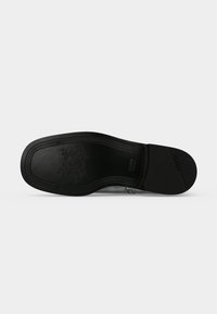 Semelle de chaussure en cuir noir avec logo embossé et couture décorative autour du bord, présentée sur un fond clair uni.