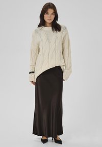 Elfenbenstrikket sweater med kabelstrikmønster, lange ærmer og en løs pasform, parret med en mørkebrun satinmaxi-nederdel og sorte spidse sko.