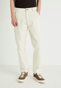 Beige cargo pants with a relaxed fit, button closure, and multiple pockets. Made of sturdy cotton fabric, featuring subtle stitching details.