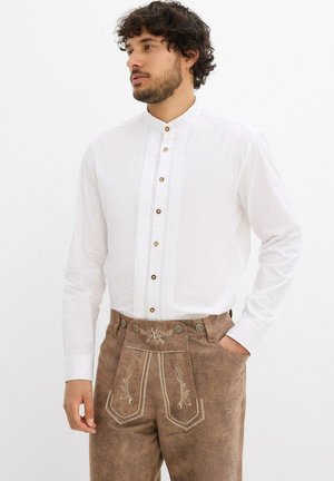 Weißes Langarmhemd mit Stehkragen, versehen mit Paspel-Details und braunen Knöpfen; kombiniert mit braunen bestickten Hosen.