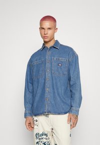 Μπλε τζιν πουκάμισο με δύο τσέπες στο στήθος, σχέδιο με κουμπιά και κολάρο. Μαλακή υφή με ορατές ραφές.