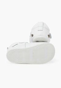 Sandali per bambini in pelle bianca con cinturini in Velcro, perforazioni sui lati e suole in gomma bianca testurizzata, caratterizzate da righe orizzontali.