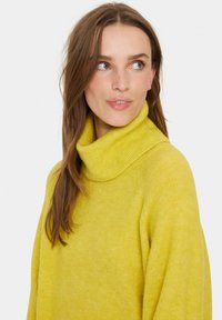 Žuta, rebrasta turtleneck dukserica s mekim materijalom i opuštenim krojem, s dugim rukavima i širokim okovratnikom.