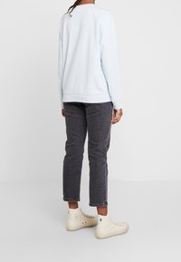 Světle modrá mikina s dlouhými rukávy, ribbenými manžetami a lemem; kombinovaná s tmavě šedými rovnými džíny a béžovými teniskami s vysokým svrškem.