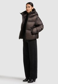 Tumepruun sulejope, millel on kõrge krae, tikitud muster ja tõmblukk, kombineeritud laia säärega mustade pükstega ning kontsakingadega.