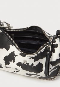 Bolso de mano con estampado de vaca que presenta un exterior texturizado en blanco y negro, cierre con cremallera, compartimentos interiores y accesorios en tono plateado.