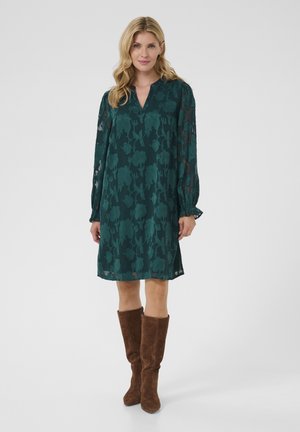 Green floral print dress with long sleeves, V-neckline, and gathered cuffs. Paired with brown suede knee-high boots.