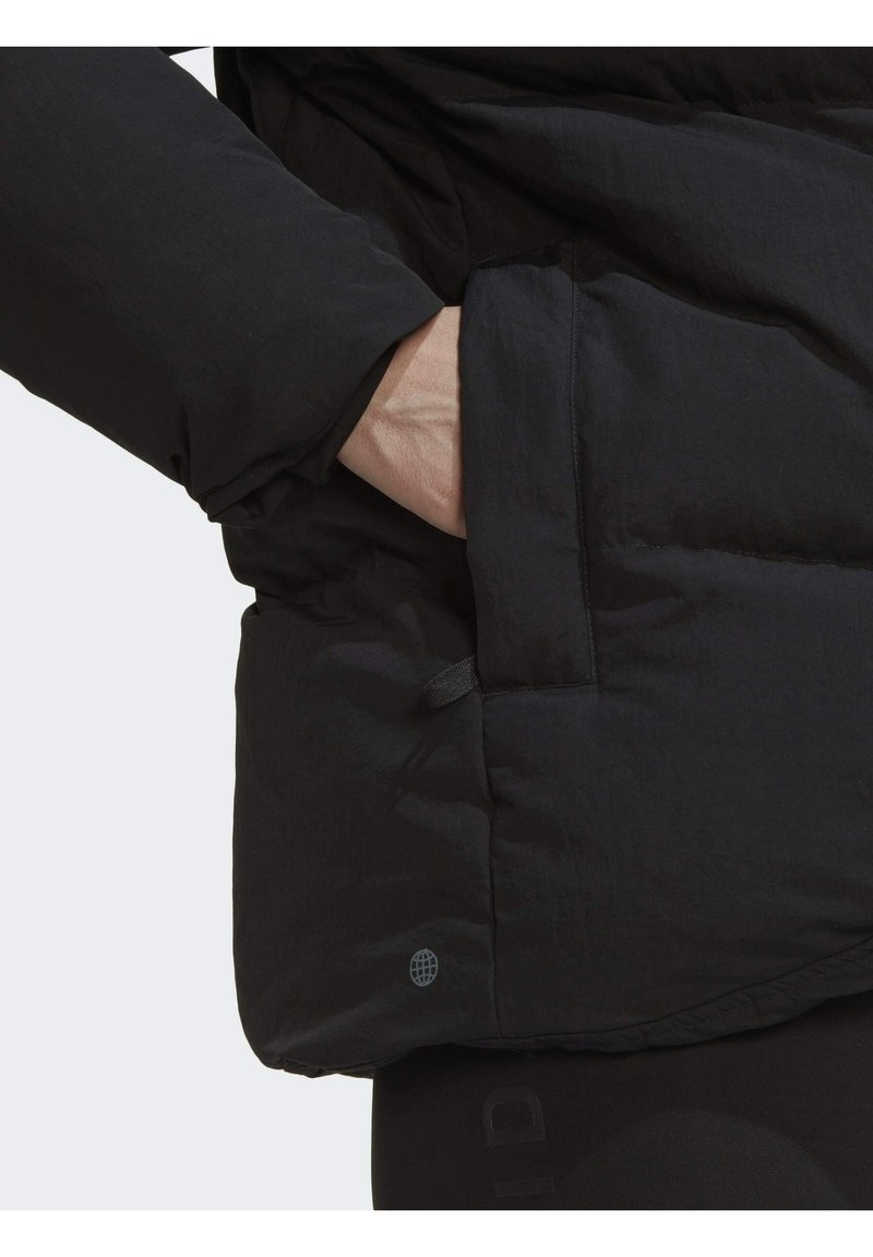 Schwarze Puffjacke aus strukturiertem Material mit seitlicher Tasche und kleinem Logo nahe dem Saum. Schlankes, modernes Design mit einer warmen Ausstrahlung.