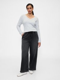 Suéter suave de color gris claro con cuello en V combinado con pantalones vaqueros oscuros de corte holgado. El modelo lleva zapatillas blancas. Diseño minimalista.