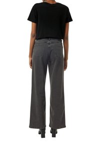 Czarny T-shirt z krótkim rękawem noszony z szarymi dżinsami o wysokim stanie i szerokich nogawkach. Dżinsy mają dwie tylne kieszenie i gładkie, teksturowane wykończenie.