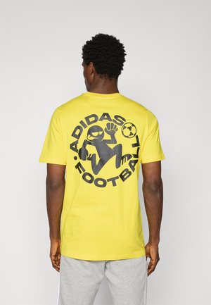 Gul bomulds T-shirt med en stor sort grafik med en fodbold og en tegneseriefigur på ryggen. Korte ærmer, afslappet pasform.