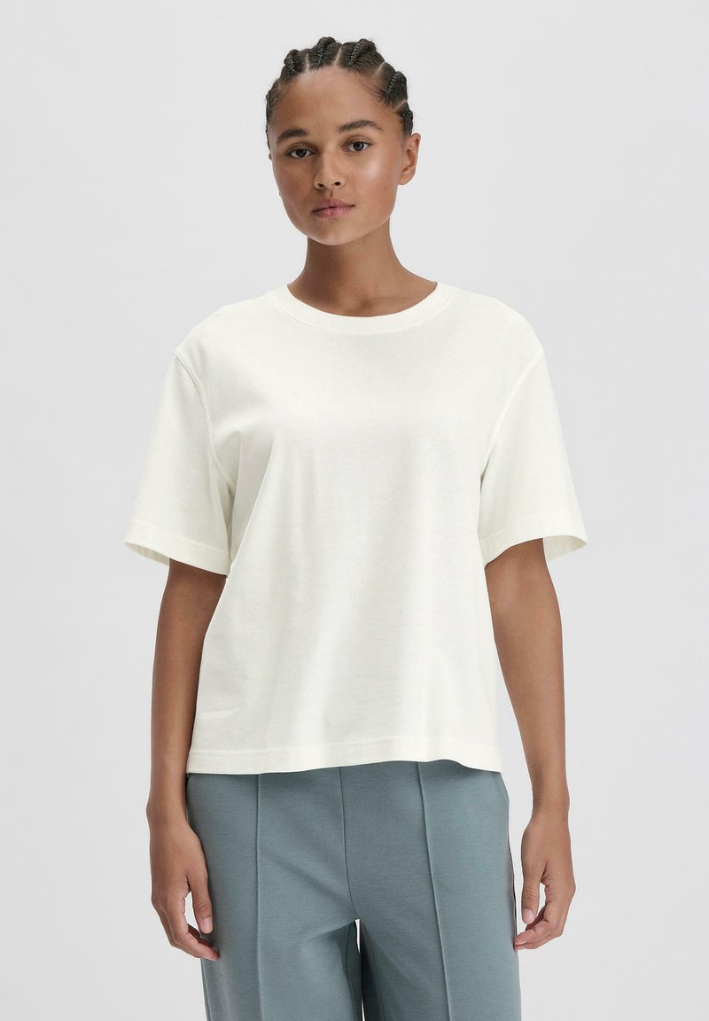 Lichtbeige korte mouw t-shirt met een ronde hals, relaxte pasvorm en zachte katoenstructuur. Gecombineerd met lichtblauwe wijde broek.