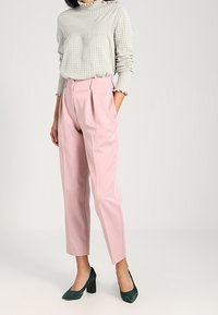Pull en laine gris clair avec un motif texturé, associé à un pantalon rose à taille haute et plis, et des chaussures à talons vert foncé.
